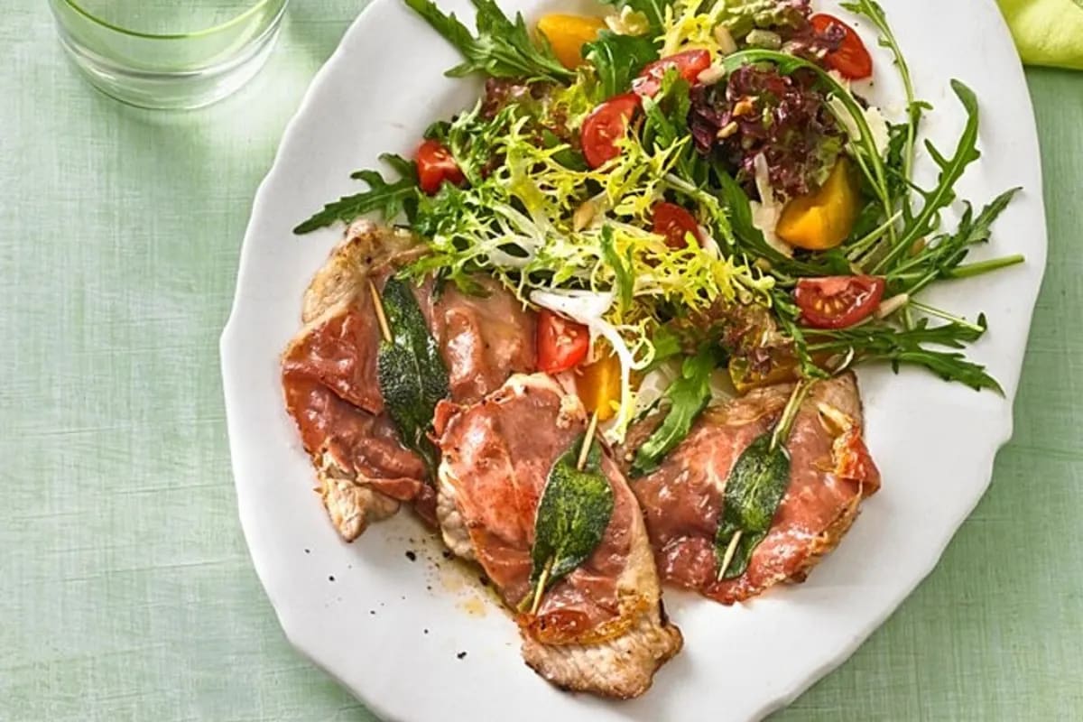 Zartes Kalbsschnitzel, belegt mit Parmaschinken und frischem Salbei, auf einem Teller mit Marsala‑Sauce