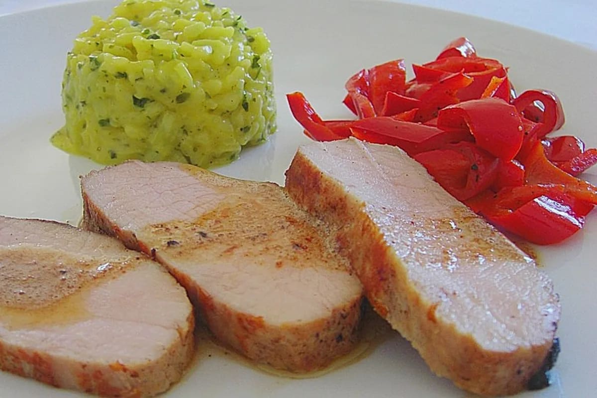 Sous Vide gegarter Schweinerücken auf Schneidebrett neben sautiertem Kohlrabi, garniert mit Kräutern