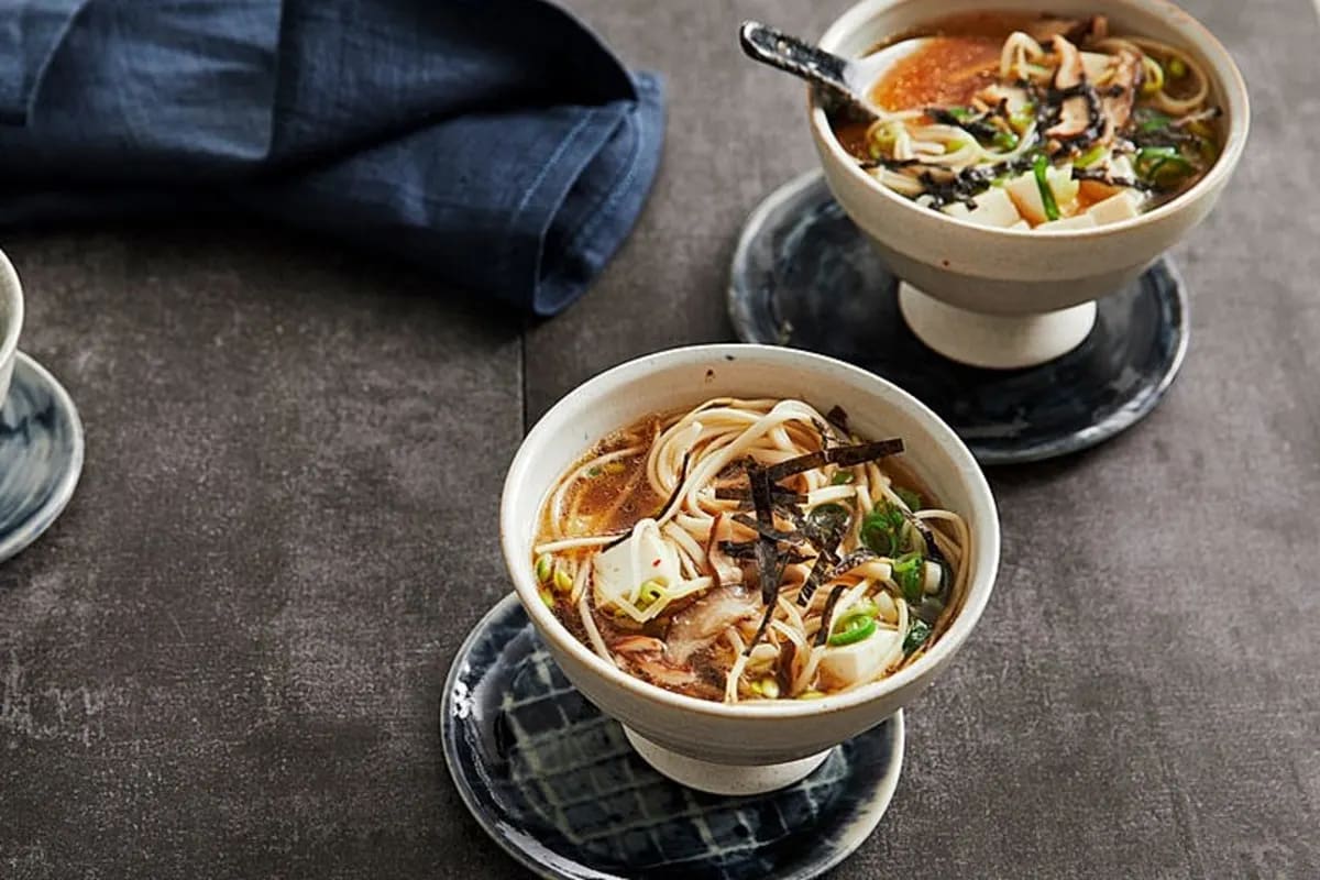 eine Schüssel dampfende Miso‑Ramen‑Suppe mit Shiitake, Tofu, Frühlingszwiebeln und Nori auf einem Holztisch