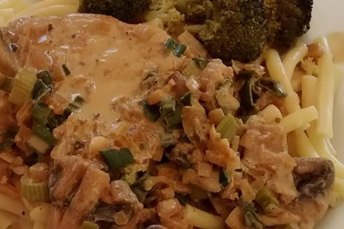 Goldbraun überbackenes Zwiebel‑Sahne‑Schnitzel mit geschmolzenem Käse, daneben knusprige Pommes und frischer grüner Salat