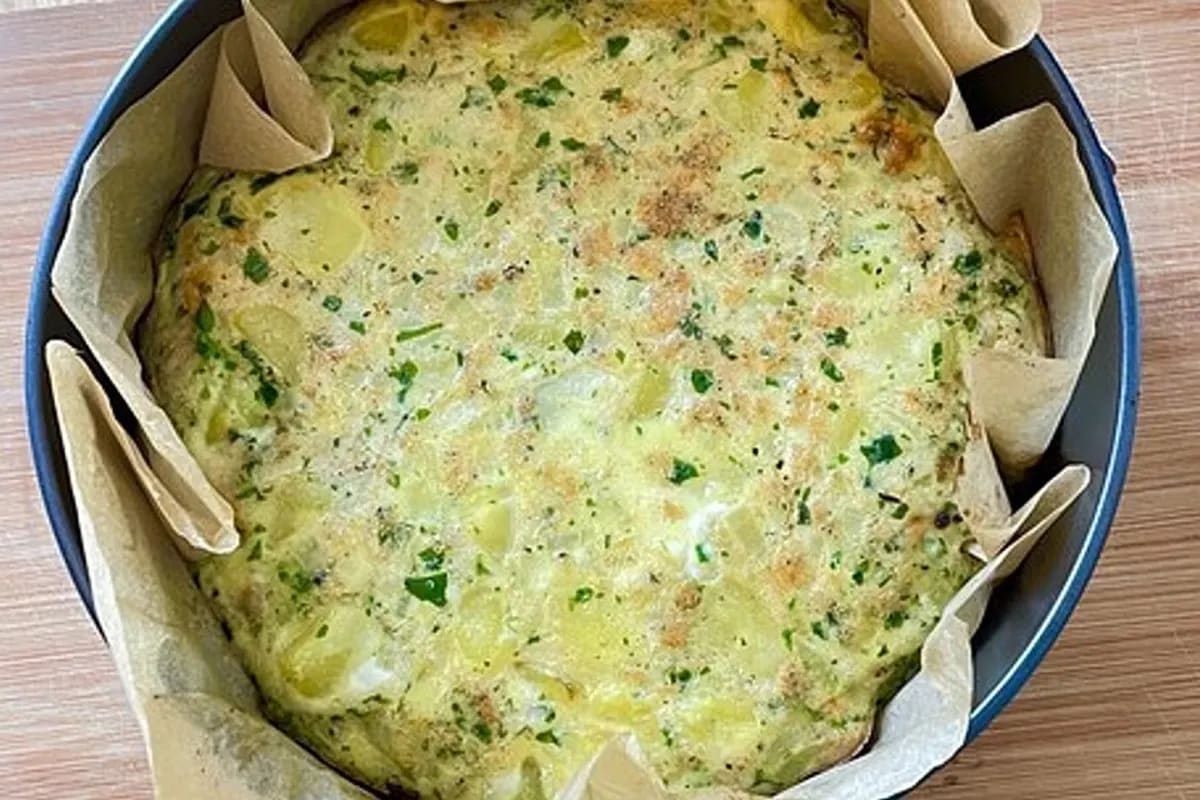 Goldbraune spanische Tortilla aus dem Backofen, in Stücke geschnitten, auf Holzbrett serviert