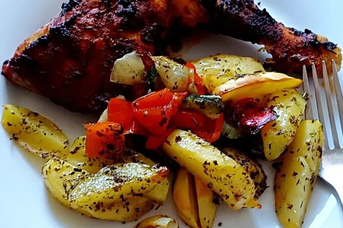Knusprig gebratene Hähnchenschlegel auf einem Blech mit gerösteten Kartoffeln, Karotten, Paprika und Zucchini