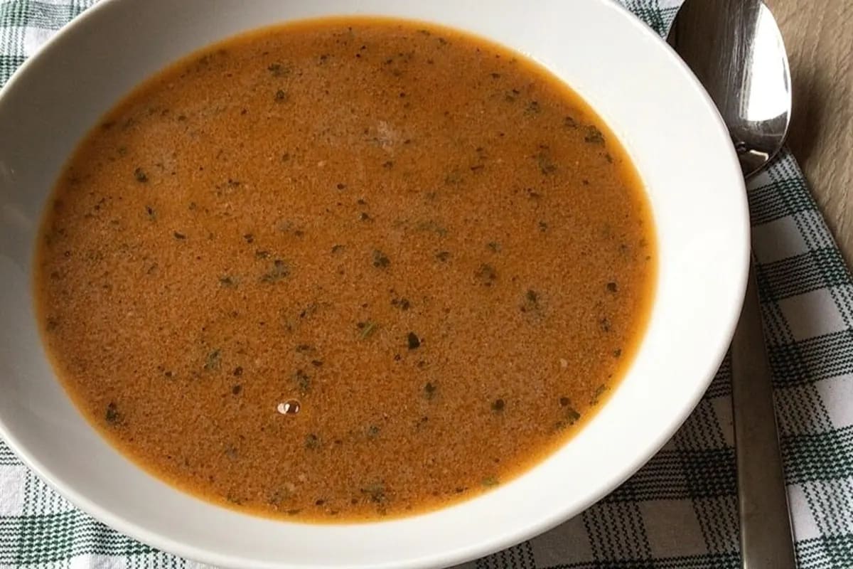 Eine dampfende Schale Wildsuppe mit Preiselbeeren, Pilzen und frischer Petersilie