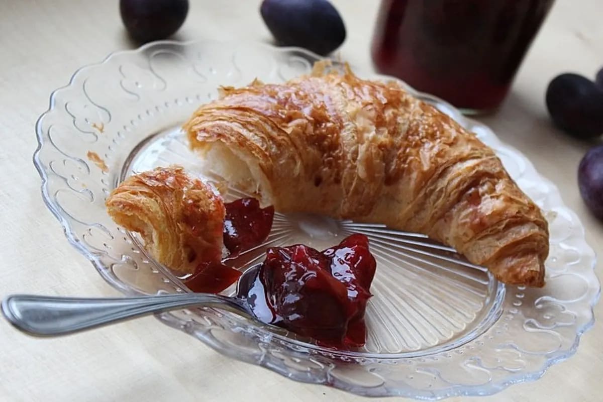 Glas mit dunkelroter Pflaumenmarmelade, verziert mit einer Zimtstange und einem Weinglas daneben