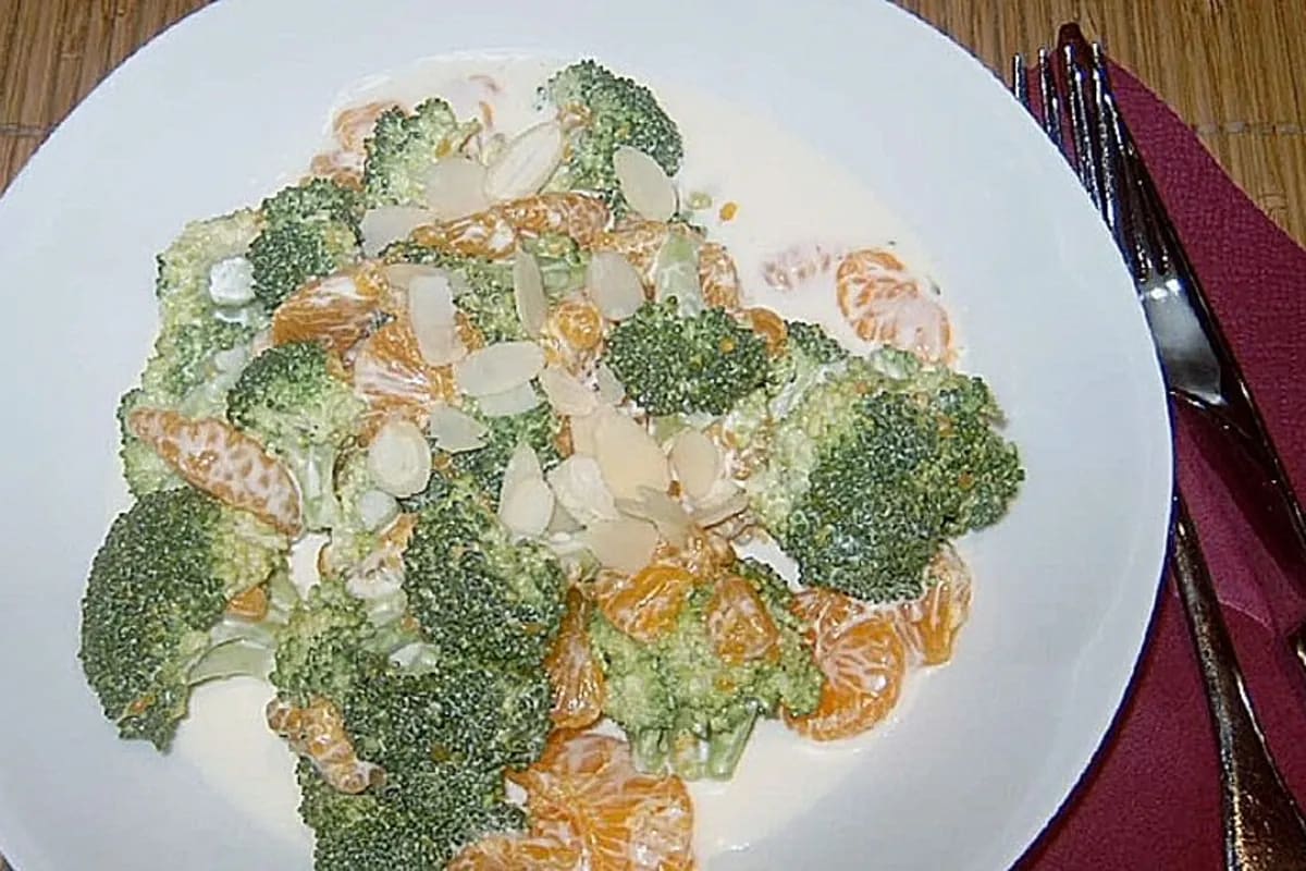 Bunter Brokkoli-Salat mit Crème fraîche, Mandarinen und gerösteten Mandeln auf einem weißen Teller