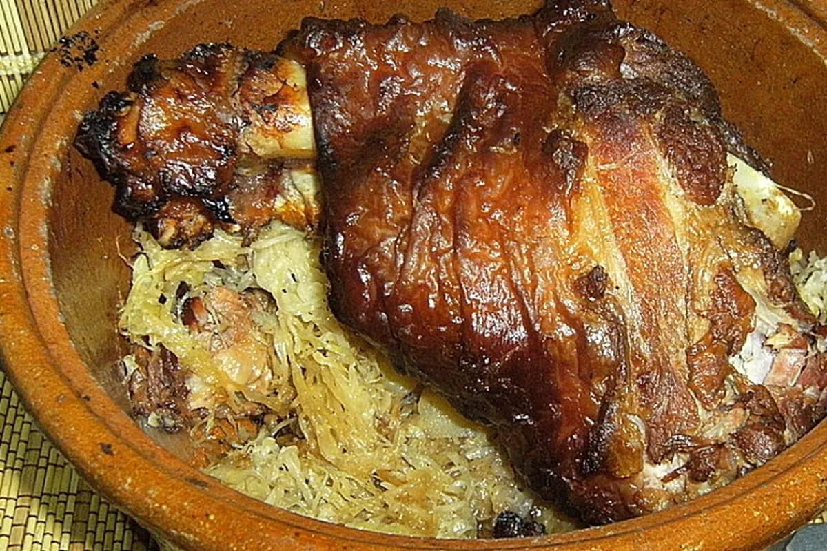 Saftige Schweinshaxe liegt auf einem Bett aus goldbraun gegartem Sauerkraut im offenen Römertopf