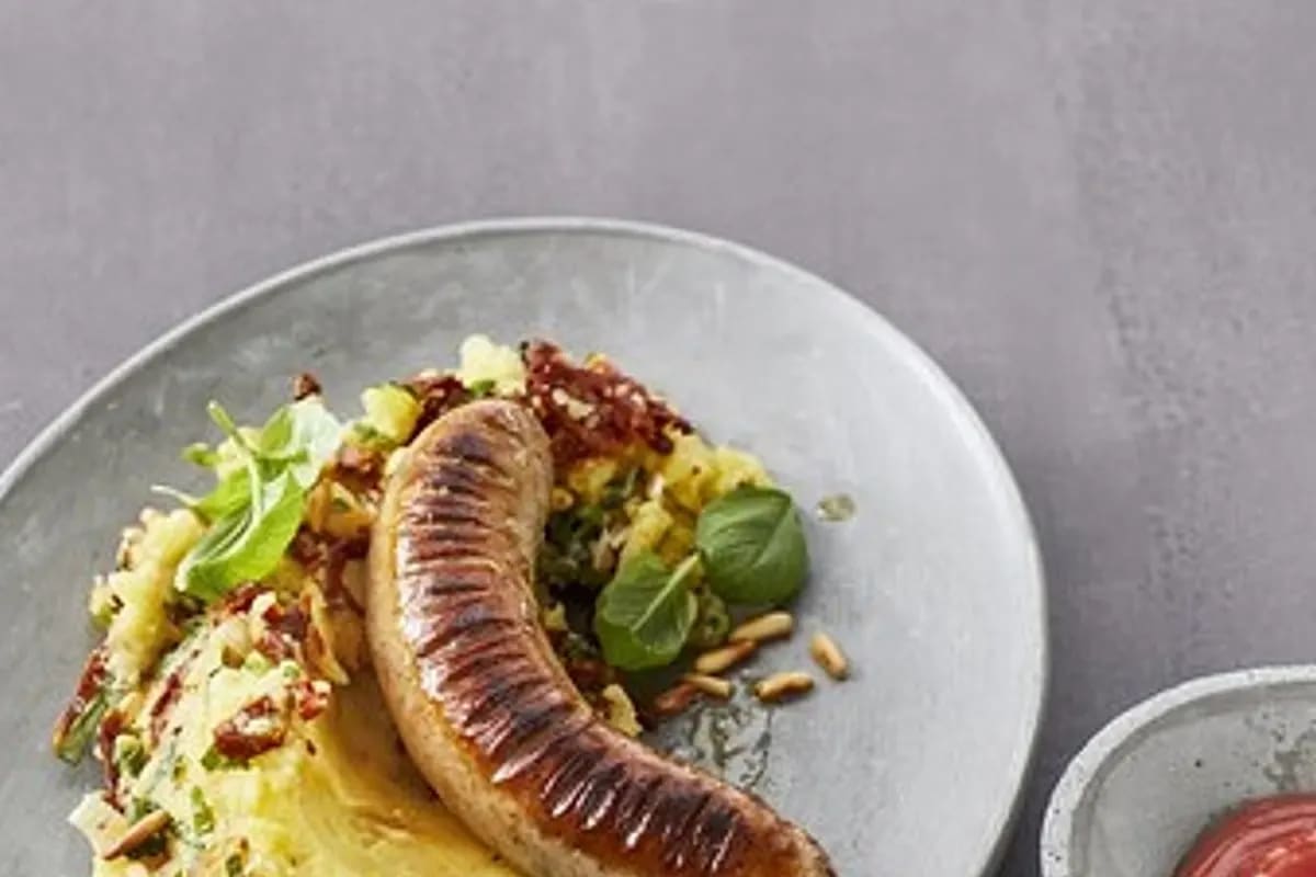 Cremiges mediterranes Blumenkohl-Püree mit gerösteten Pinienkernen, getrockneten Tomatenstreifen und frischem Basilikum auf einem rustikalen Holzbrett