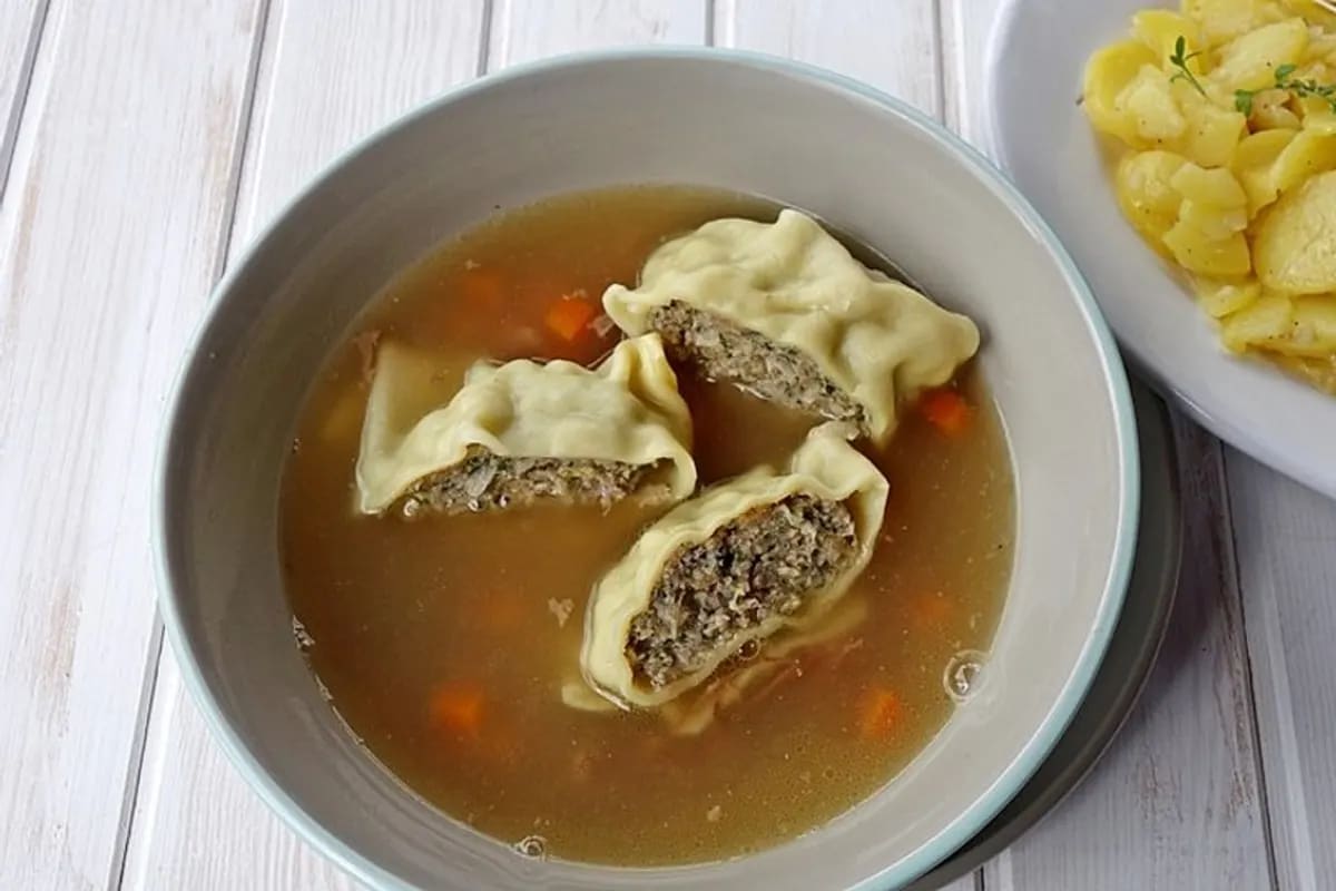 Gerollte Maultaschen auf einem Holzbrett, leicht gebräunt, mit frischer Petersilie bestreut