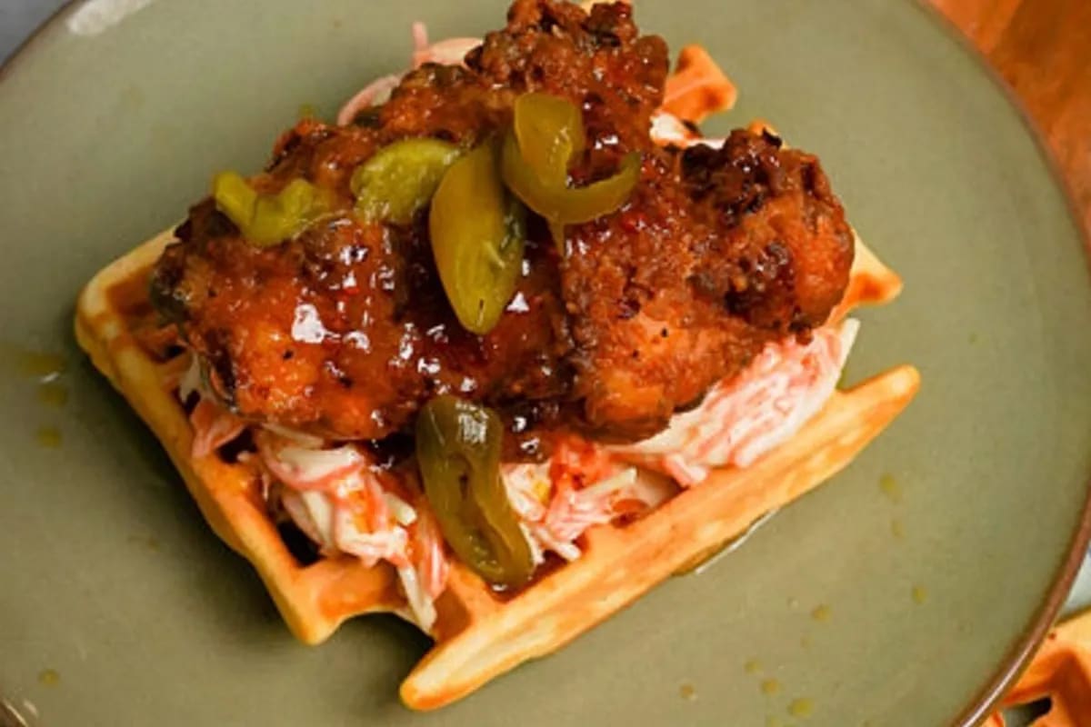 Knuspriges frittiertes Hähnchenstück auf einer goldbraunen Waffel, garniert mit schmelzender Ahorn‑Chili‑Butter und frischem Cole Slaw