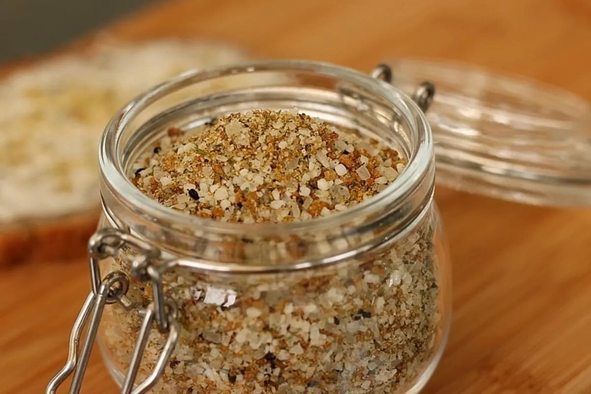 Ein Glas mit selbstgemachtem Butterbrotsalz neben frischem Bauernbrot und einer Butterstulle
