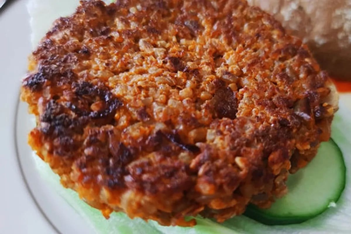 Goldbraun gebratene Grünkern‑Patty mit knuspriger Oberfläche, daneben ein kleiner Haufen Haferflocken