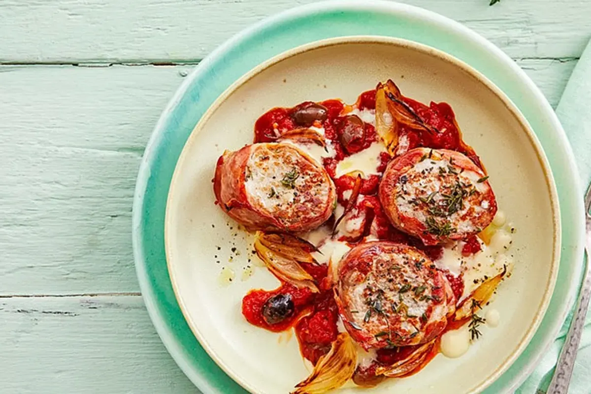 Saftige Schweinefilet-Medaillons, eingewickelt in Parmaschinken, in roter Tomaten‑Sahne‑Sauce, garniert mit Oliven und frischem Basilikum
