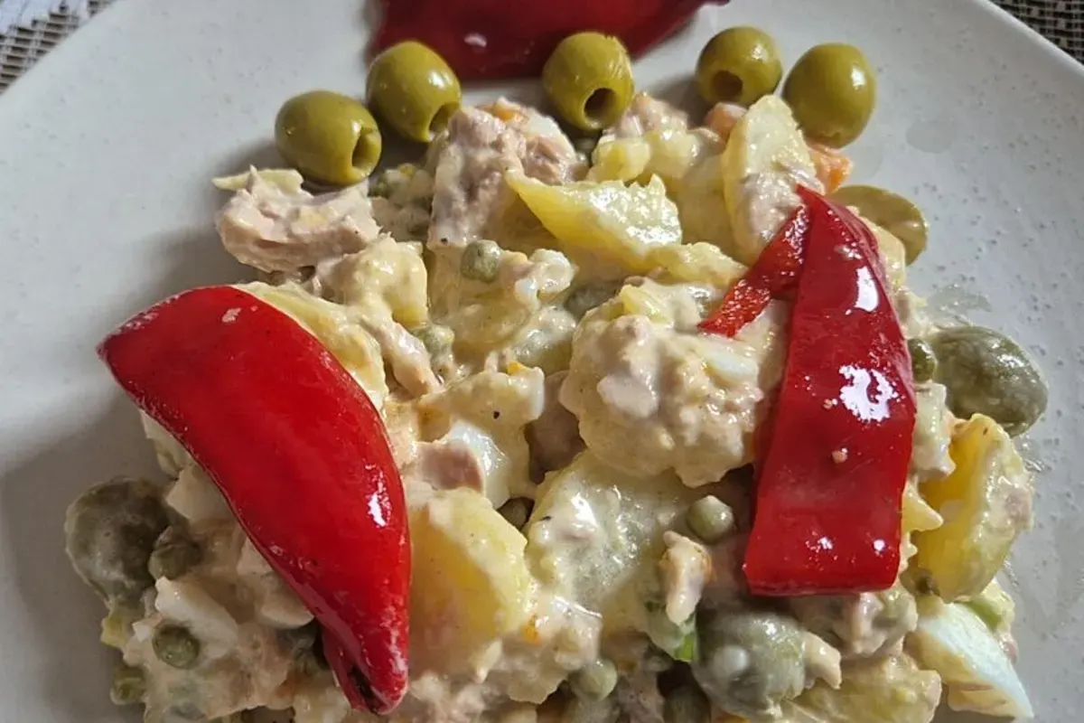 Bunter spanischer Kartoffelsalat mit Oliven, Möhren und Thunfisch auf rustikalem Holzbrett