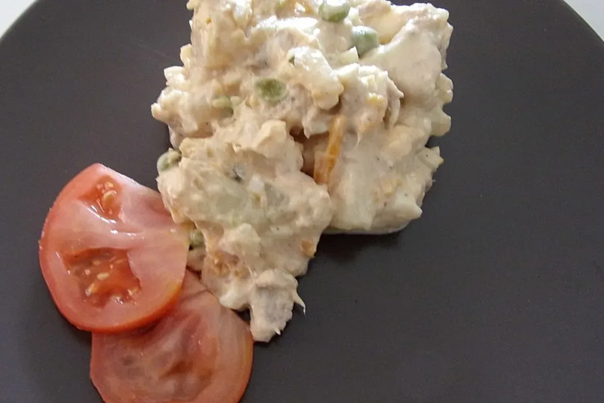 Bunter spanischer Kartoffelsalat mit Thunfisch, Oliven und frischem Gemüse auf einem rustikalen Holzbrett