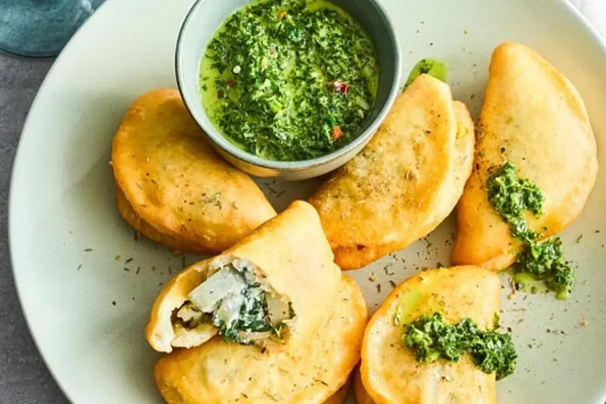 Knusprige halbmondförmige Empanadas mit leuchtend grüner Petersiliensoße auf Holzbrett