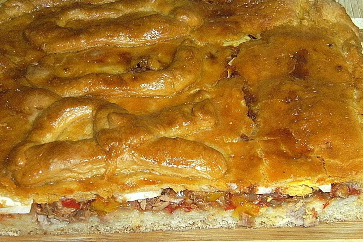 Goldbraun gebackene Empanada de Atún mit glänzendem Ei‑Guss und dekorativen Teigröllchen