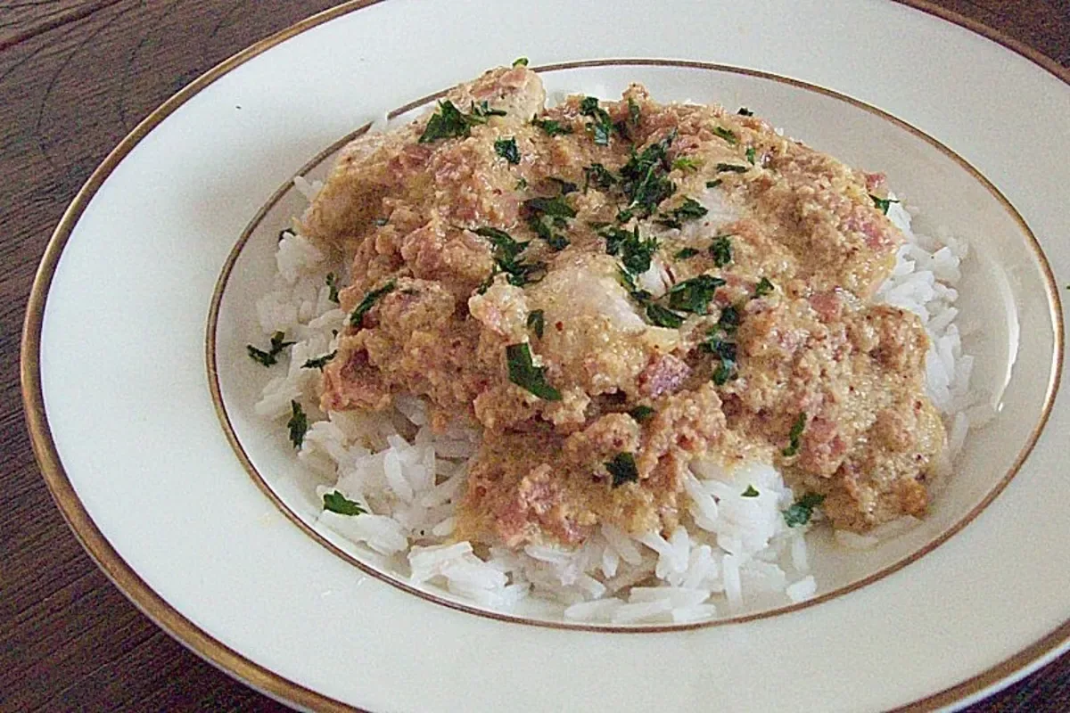 Goldbraun überbackenes Putenschnitzel mit geschmolzenem Käse, knusprigem Schinken und karamellisierten Zwiebeln auf einem weißen Teller