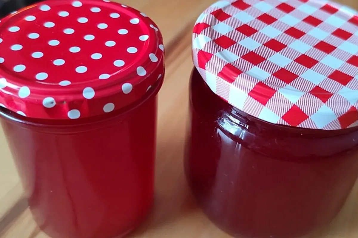 Gläser mit goldgelber Mirabellenmarmelade, daneben frische Mirabellen und Vanilleschote auf rustikalem Holztisch