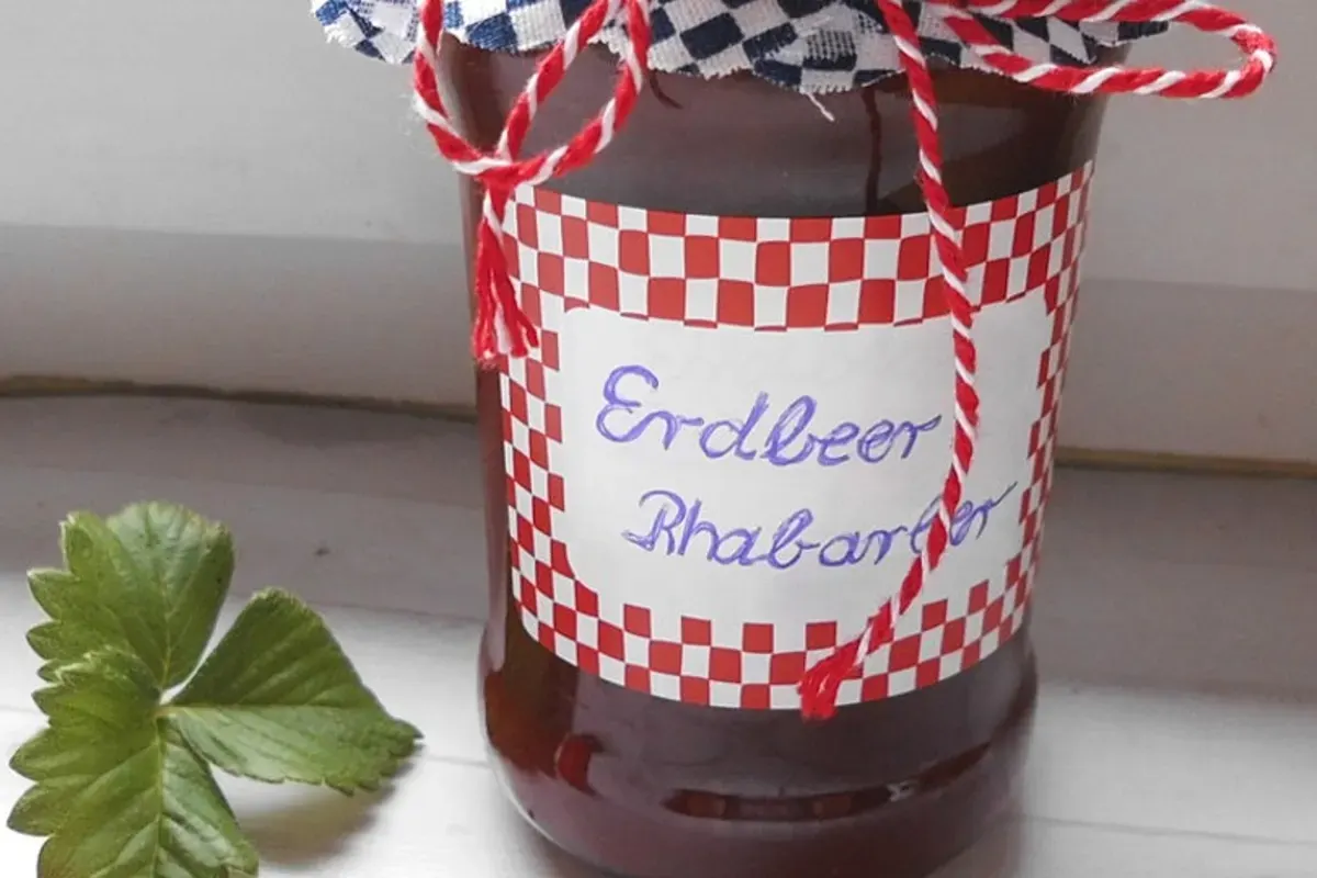 Glas mit leuchtend roter Rhabarber-Walnuss-Marmelade, daneben ein Zweig frischer Walnüsse