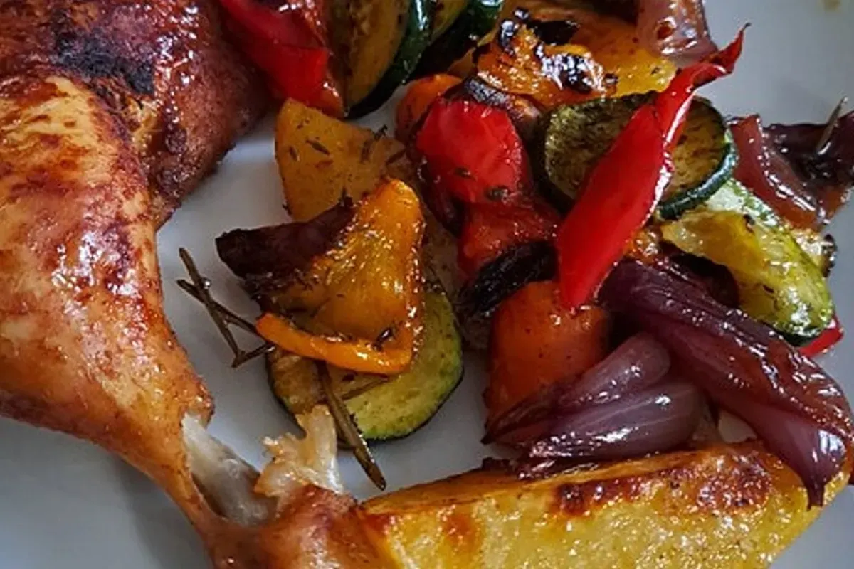 Knusprige Hähnchenschenkel auf einem Bett aus geröstetem Ofengemüse, goldbraune Haut glänzt