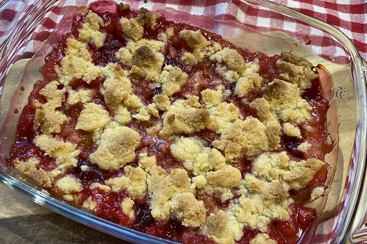 Goldbraune Streusel über leuchtend rotem Rhabarber in einer Auflaufform, daneben ein Klecks Vanilleeis