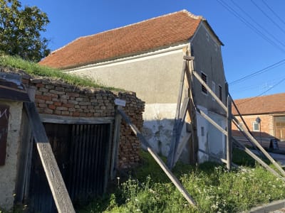 Boční náhled na průčelí a přilehlý objekt s detailním pohledem na konstrukci dřevěného pažení/vzpěr zajišťujících stabilizaci objektu.