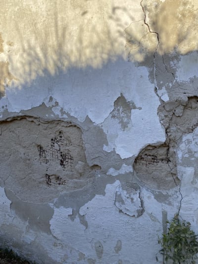 Detail degradace fasády a vápenné omítky s patrnými prasklinami a odhalenými vrstvami zdiva.