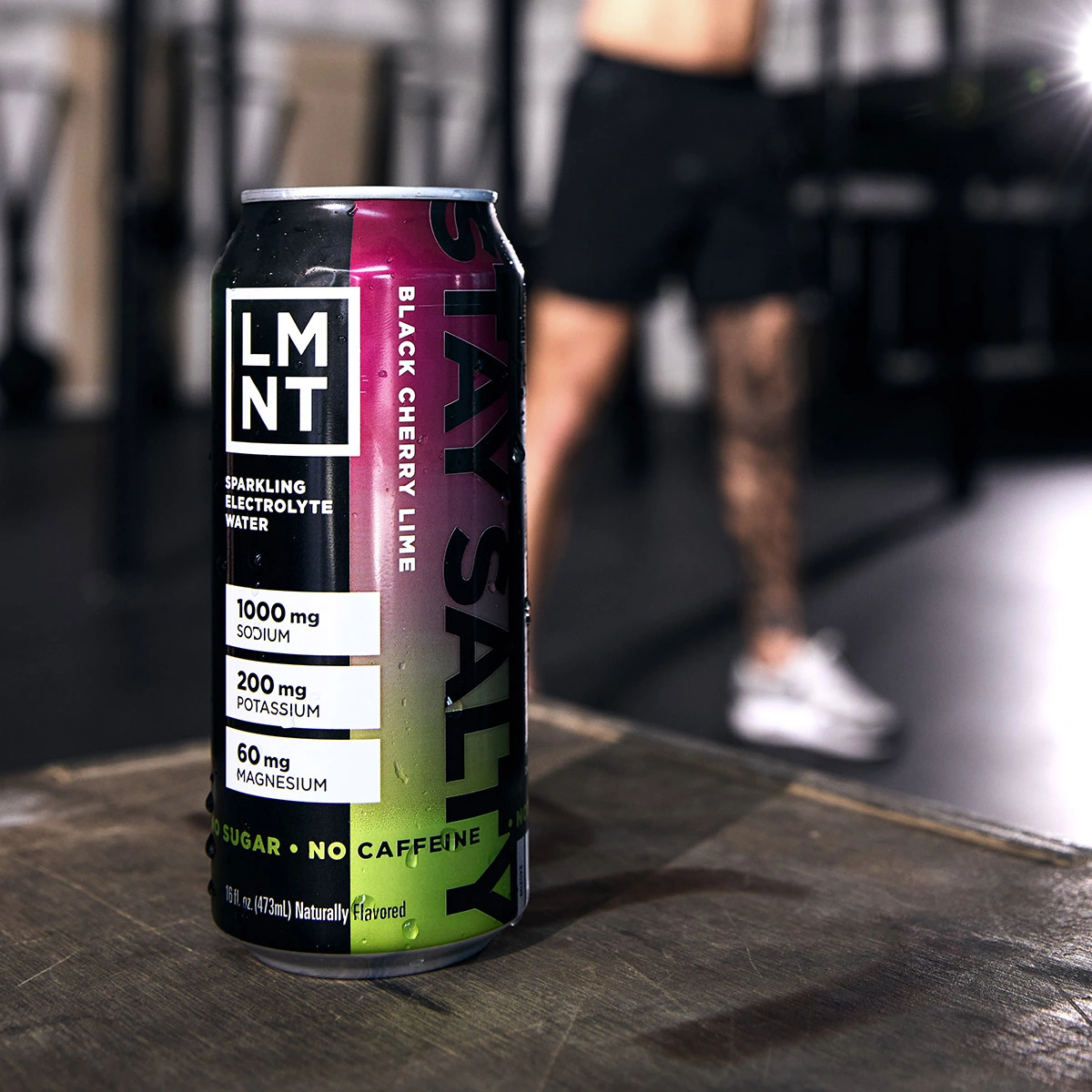 Black Cherry Lime sparkling electrolyte drink can on a gym bench with athlete nearby.