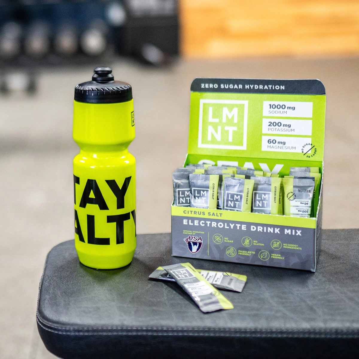 LMNT Citrus Salt drink mix and yellow 'Stay Salty' bottle on gym bench.