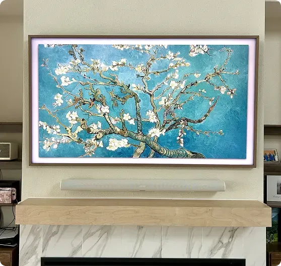 A framed screen above a fireplace displays Van Gogh's "Almond Blossom" painting, featuring blossoming branches against a blue background.