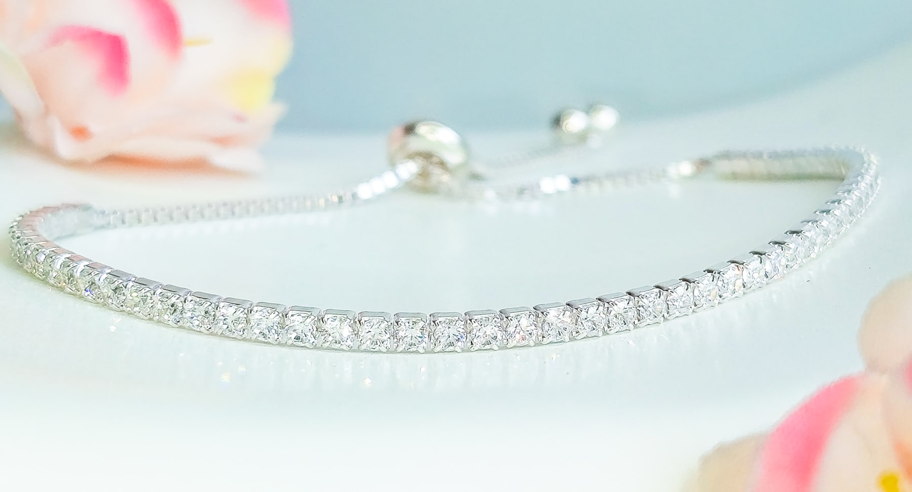 Pulsera de plata con circones brillantes sobre una superficie clara, junto a flores rosadas