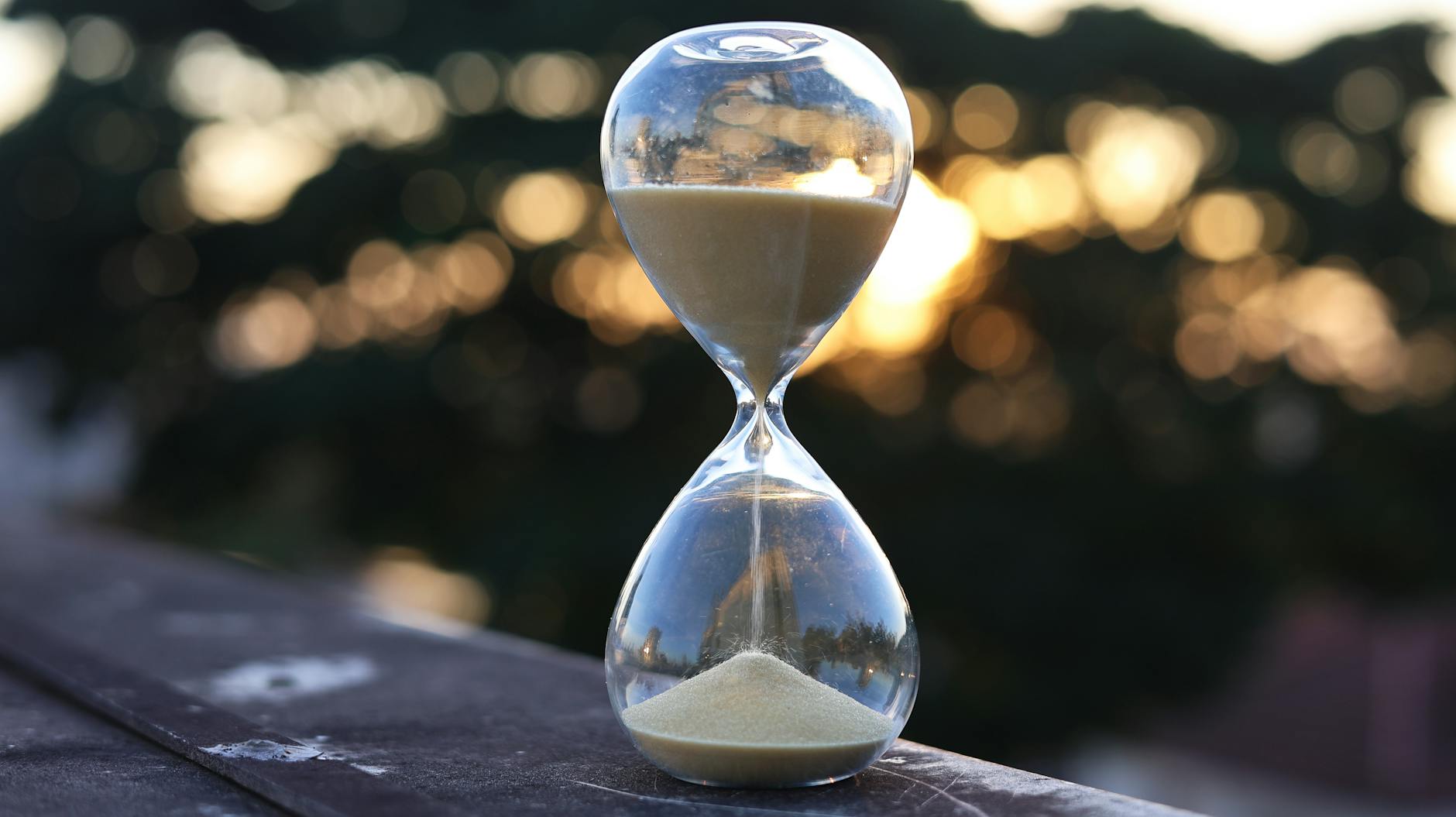 Reloj de arena al atardecer, sol filtrándose entre los árboles