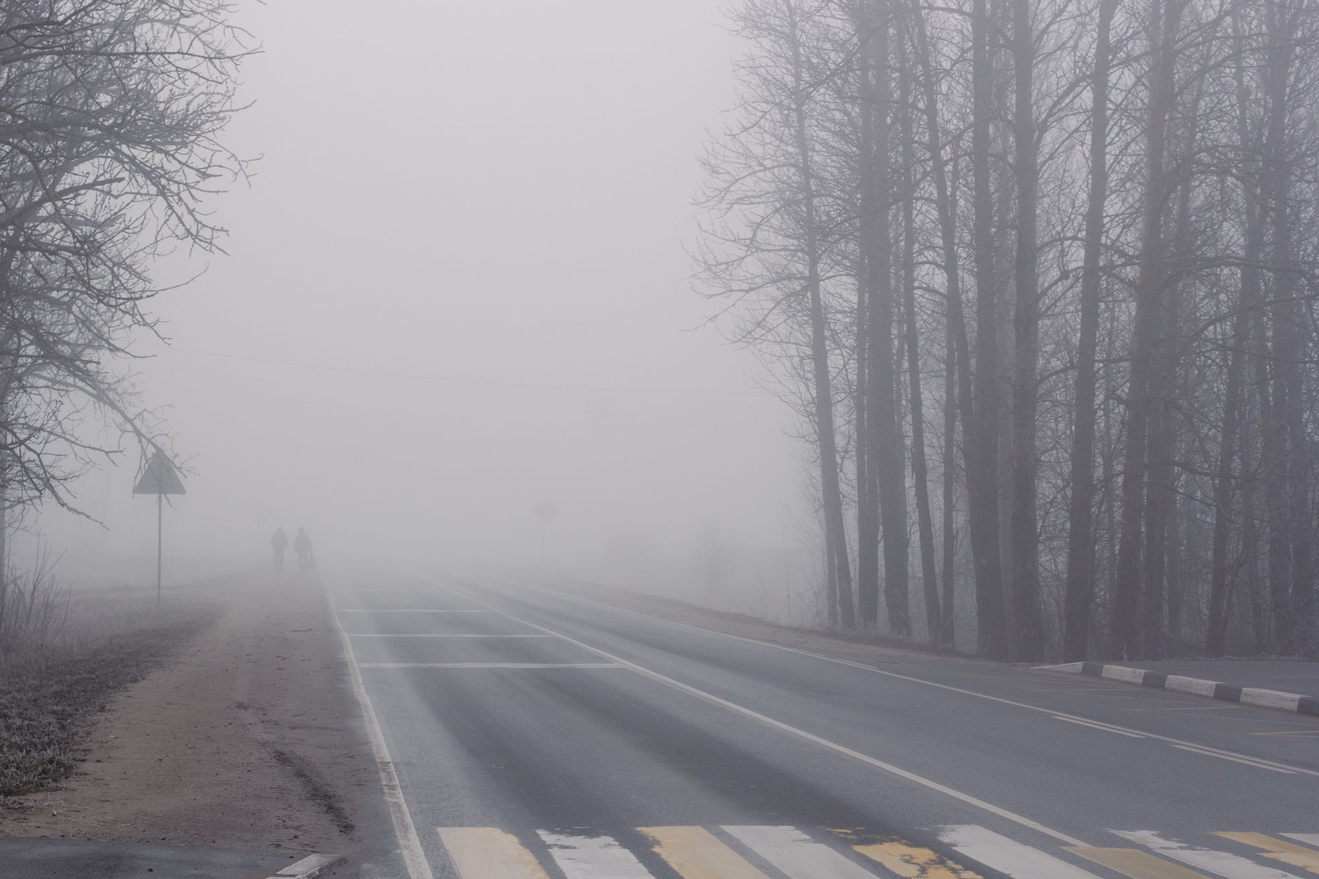 Carretera entre niebla con dos figuras caminando a lo lejos