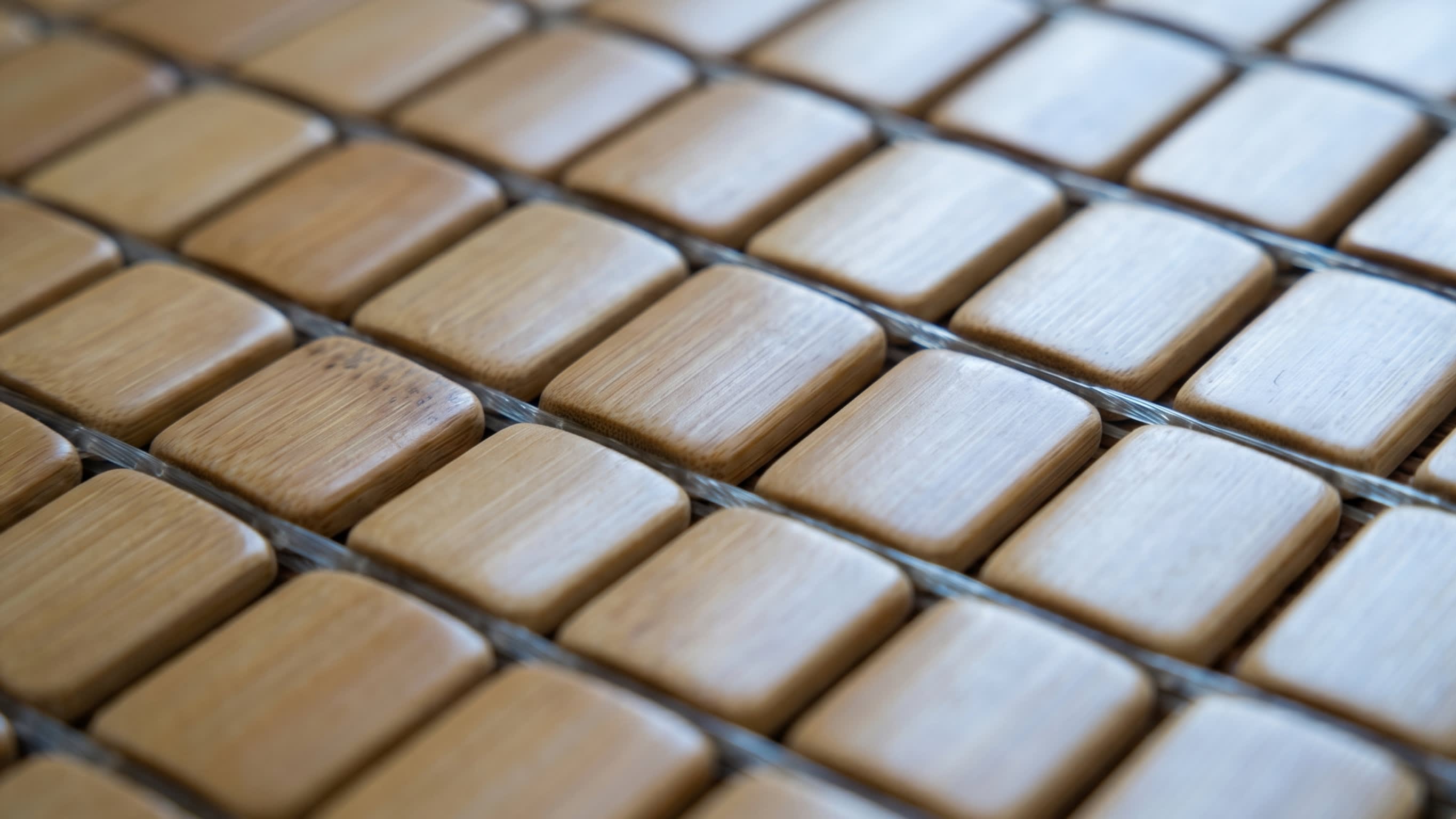 A detailed macro shot showing the smooth, polished rectangular bamboo tiles of a Chinese Mahjong sleeping mat, laced together with clear heavy-duty fishing line (16:9 ratio)