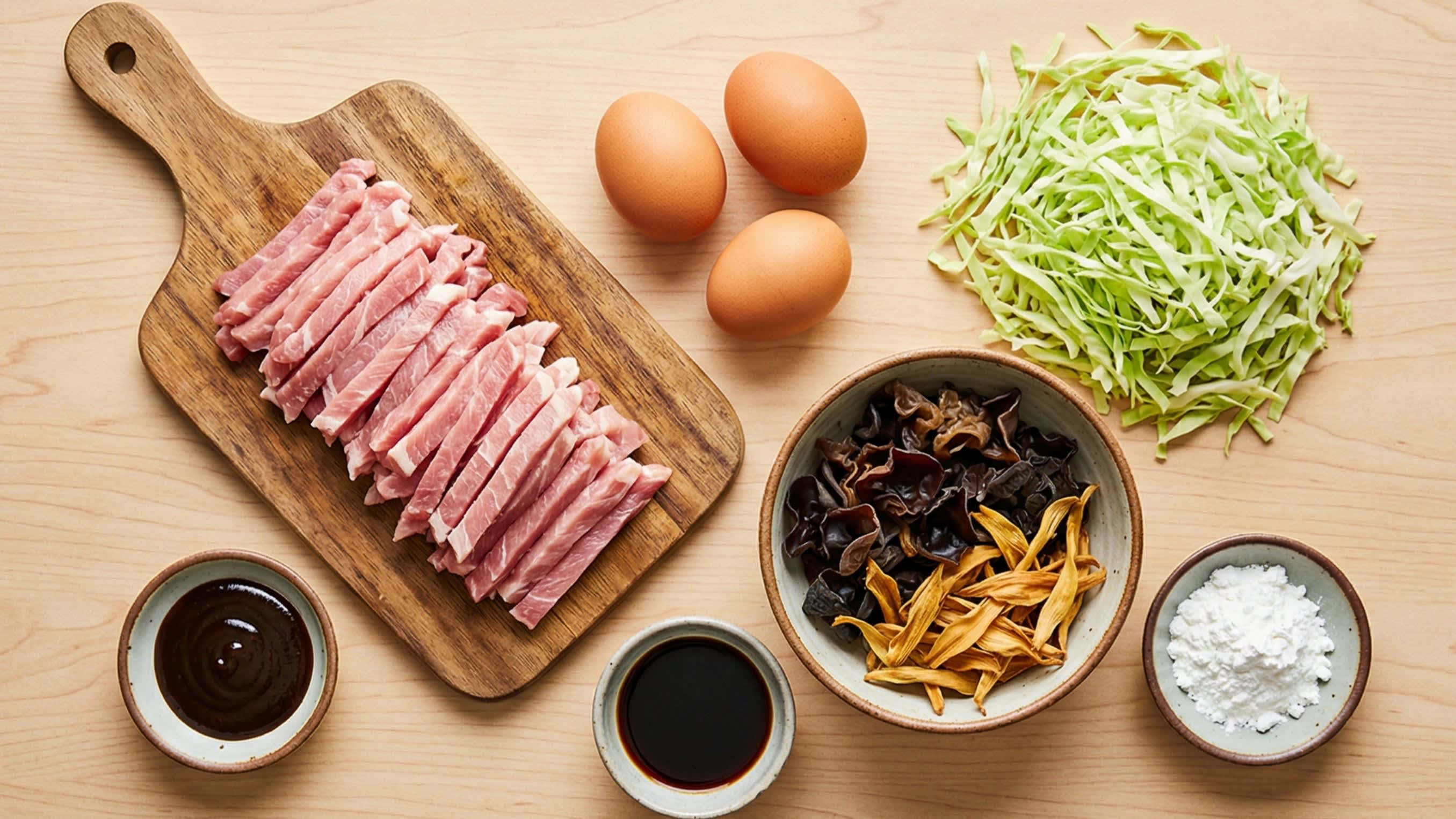 A beautiful flat lay of fresh ingredients on a wooden board: raw pork strips, fresh eggs, shredded green cabbage, a bowl of dark, crinkly rehydrated Wood Ear mushrooms, dried golden lily flowers, scallions, and a small jar of thick Hoisin sauce.