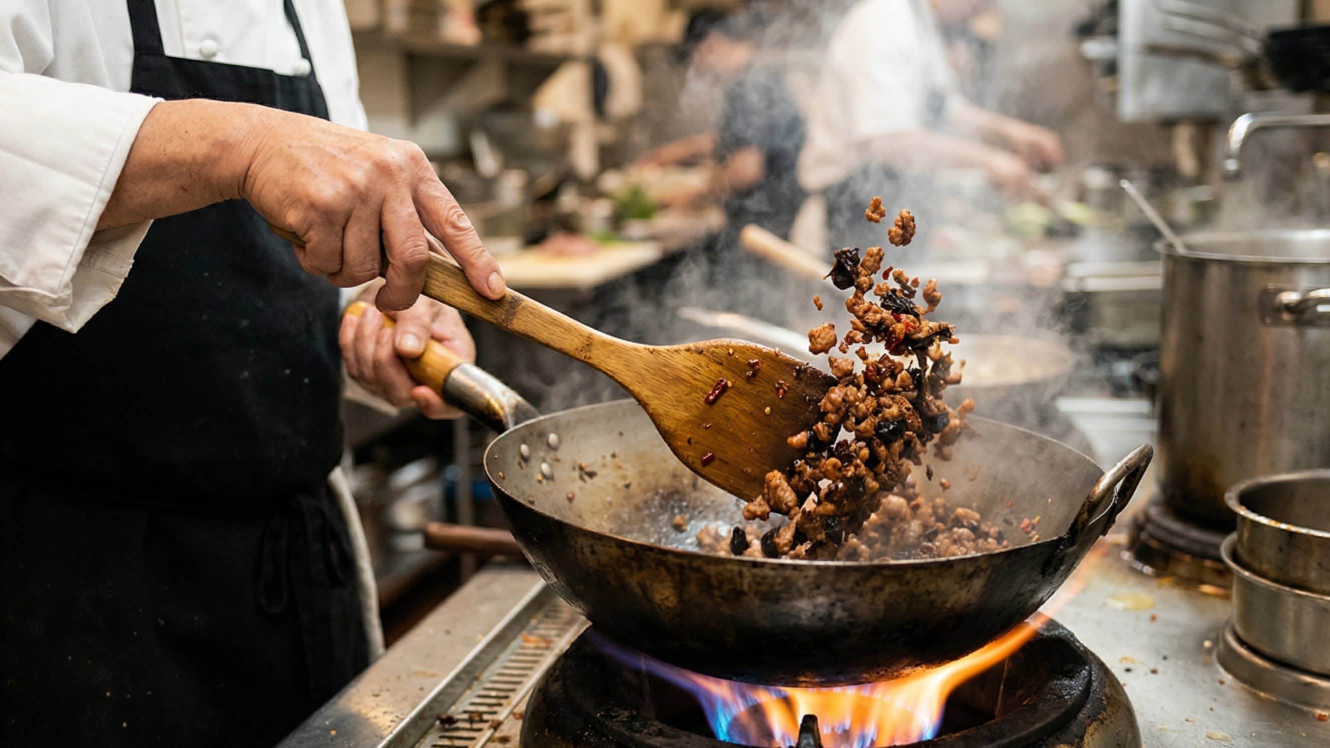 A dynamic close-up action shot looking down into a hot, well-seasoned carbon steel wok. A chef is using a wooden spatula to aggressively stir-fry finely minced ground pork until it is dark, crispy, and beautifully caramelized, mixed with the dark, savory fermented Yacai. Steam is rising.