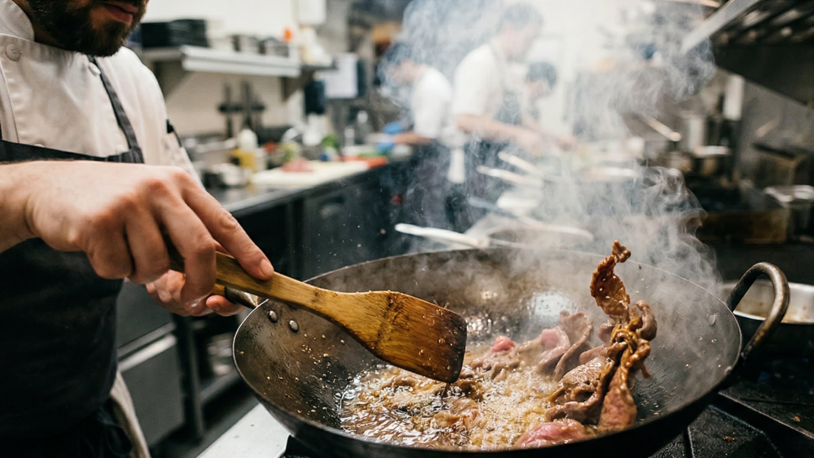 A dynamic cooking action shot inside a hot carbon steel wok. A chef is using a wooden spatula to quickly sear velvety slices of beef in bubbling hot oil. The edges of the beef are turning a beautiful brown, and the wok is filled with appetizing smoke.