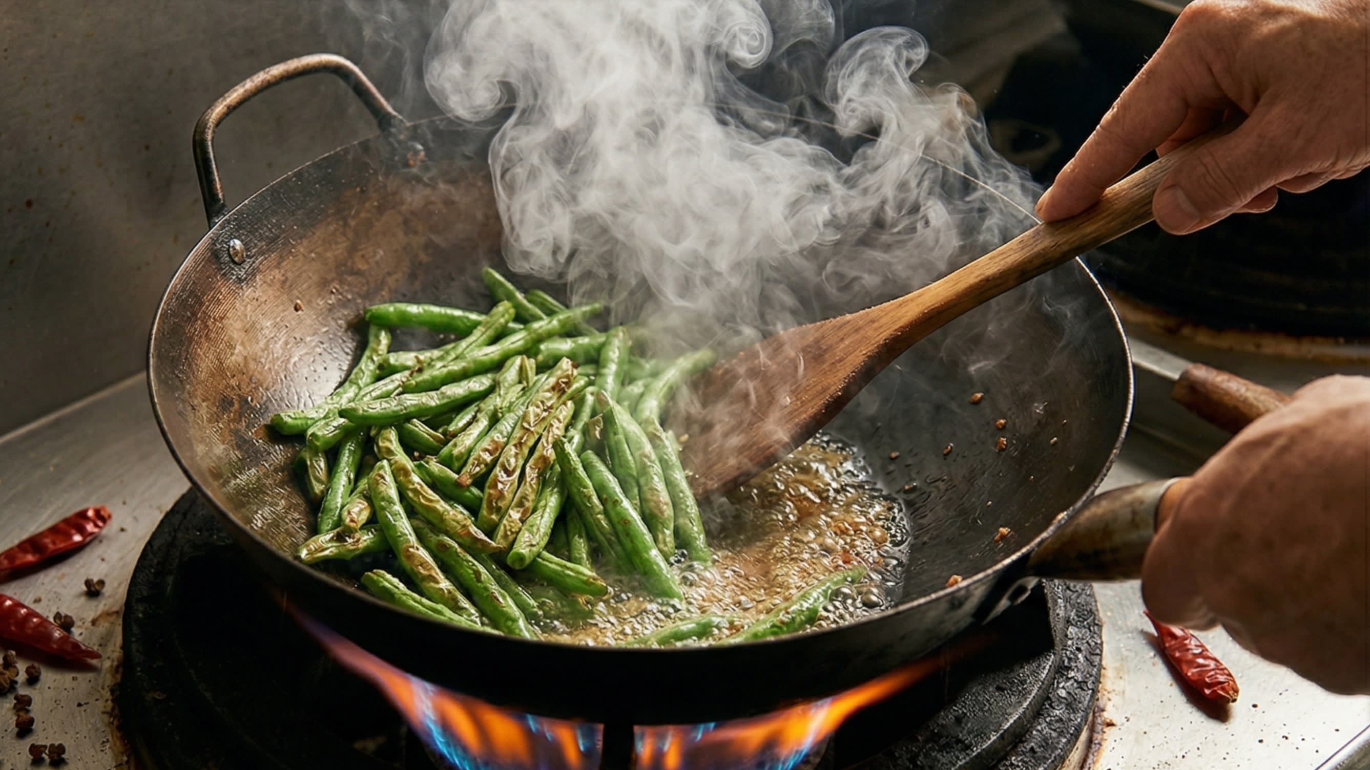 A dynamic close-up action food photography shot looking down into a hot, well-seasoned carbon steel wok. A chef is using a wooden spatula to shallow-fry bright green beans in hot oil. The skins of the green beans are visibly bubbling, shriveling, and developing beautiful, appetizing, slightly charred "Tiger Skin" blisters. Intense heat.