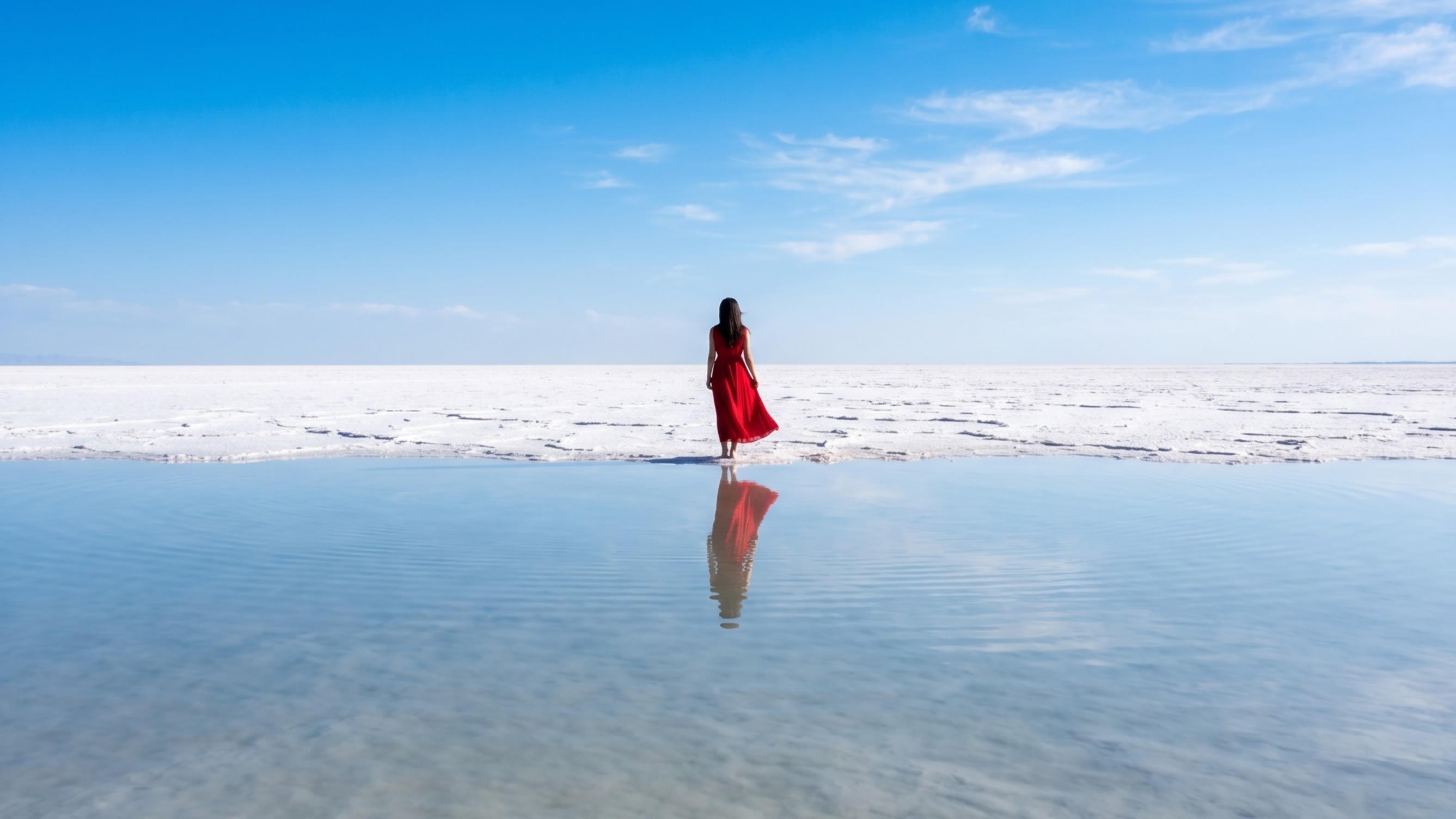 A sharp, symmetrical silhouette of a traveler standing in the reflective salt water