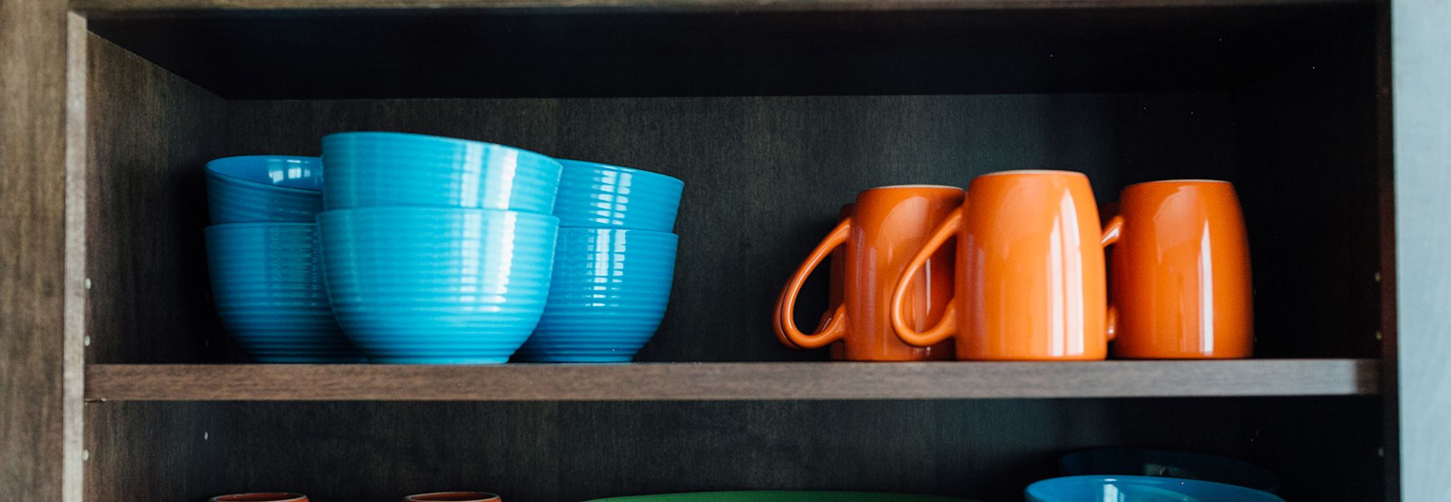 Blue dishes and orange cups are sitting on a shelf in the kitchen.