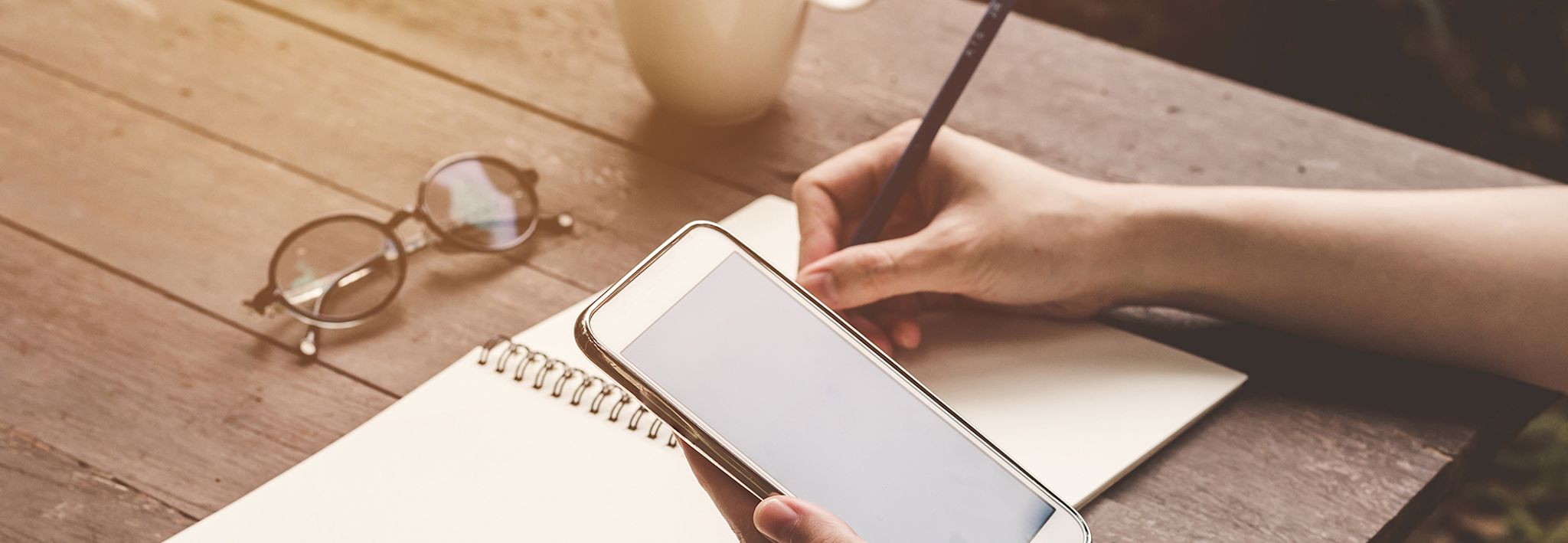 A woman is communicating on her phone while taking notes.