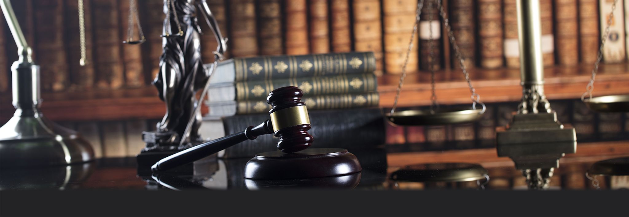 A gavel is sitting on a desk with the Lady Justice statue. 