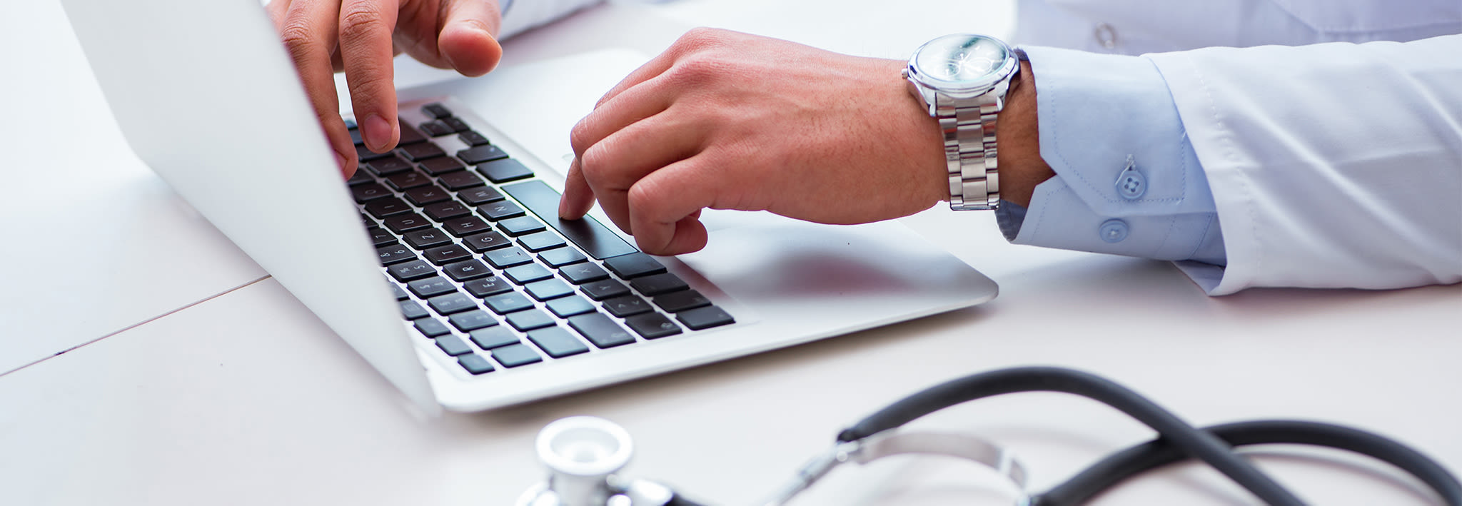 Medical professional typing on laptop computer with stethoscope in the foreground