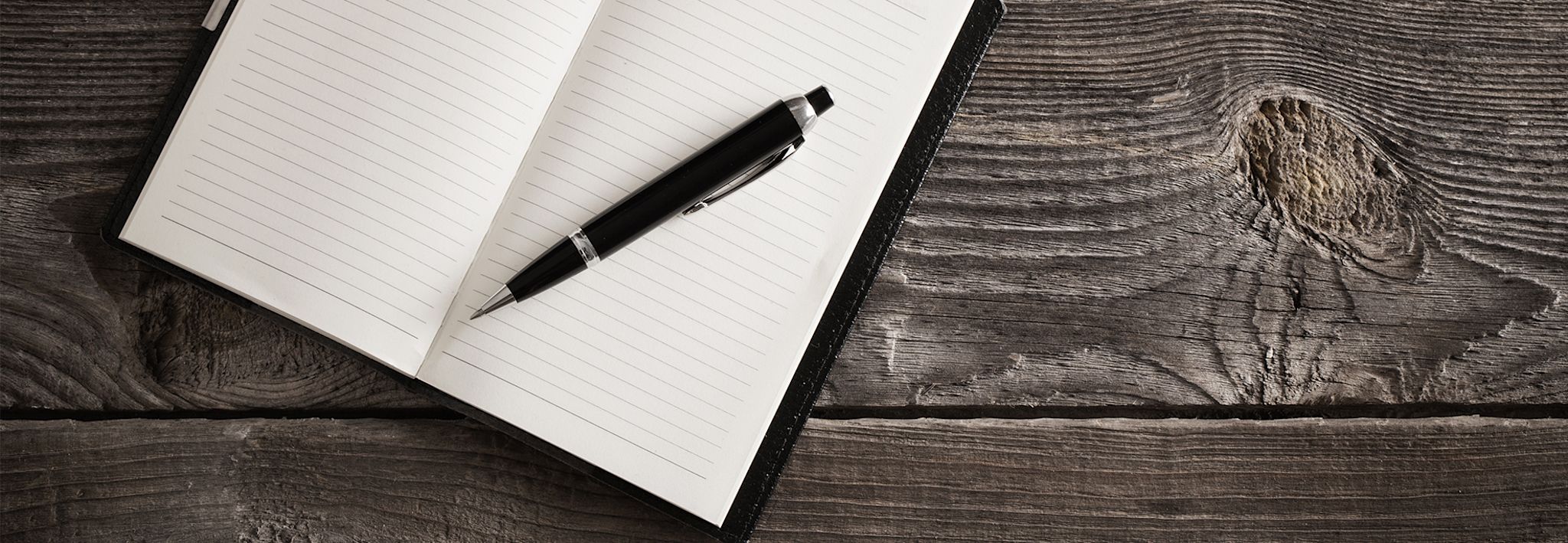 A pen and a notepad are laying on a wooden table.