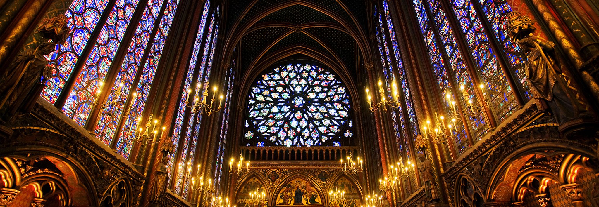 A historical church has stained glass and candles throughout it.