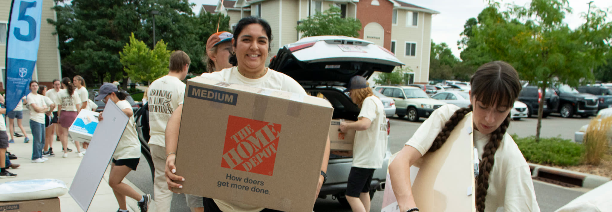 two ccu students carrying a box into a campus apartment