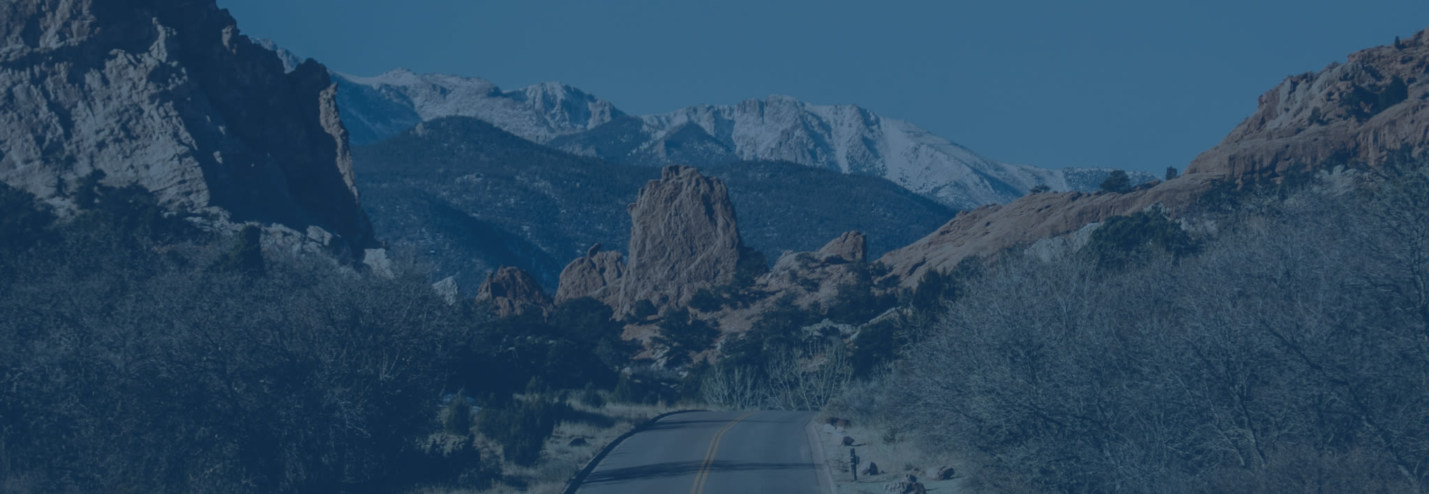 Widescreen image of a two-lane mountain road, twisting its way through the valleys and peaks of the Colorado Rocky Mountains.