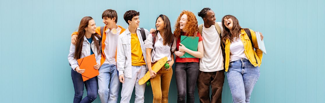 Six male and female highschool students smile and stand together against a blue wall (slide 2 of 5)