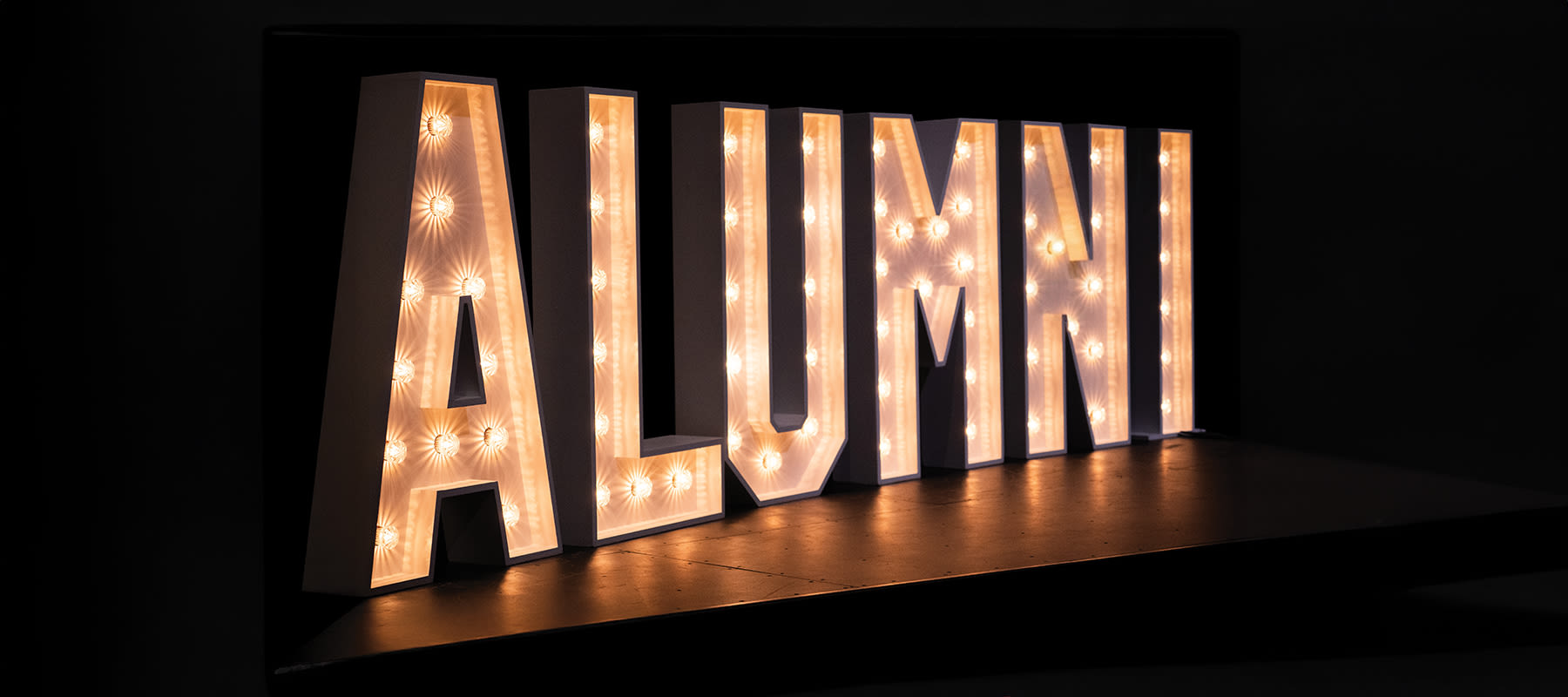 long rectangular image of glowing letters that spell out alumni