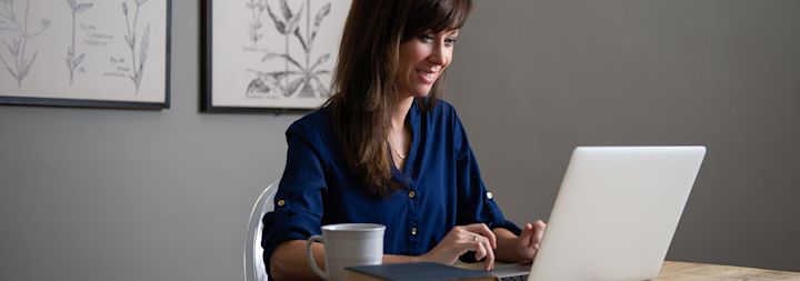 A woman takes notes with a pen next to her laptop.